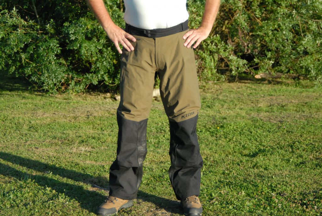 La vue de face du pantalon Klim Traverse permet de voir le grand empiècement de cuir et la coupe ample des jambes.