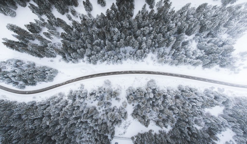 route de montagne bordée de neige et de sapins vue de drône