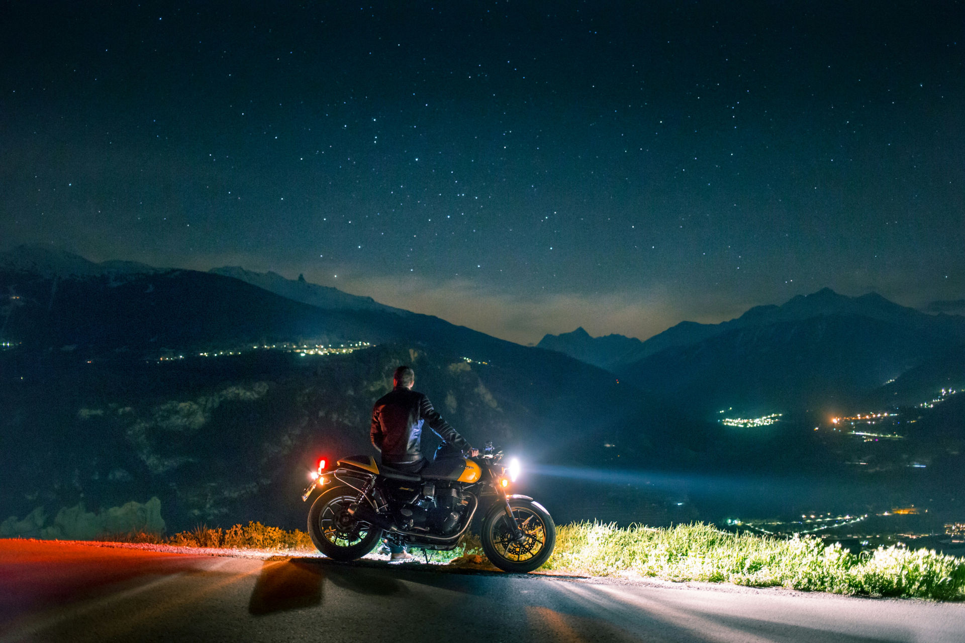 Motard posant sur sa moto devant un paysage de montagne grandiose à la tombée de la nuit, le permis moto finance par son compte personnel de formation en poche